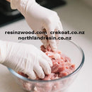 Hands in white gloves handling raw meat in a glass bowl on a kitchen counter.