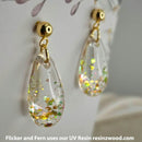 Teardrop-shaped earrings with glittery interior on a white background, featuring Flicker and Fern branding.