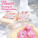 Flower drying and preservation kit shown with a white plastic bottle, two wrapped blocks of dried flower material, and a clear container holding preserved pink flowers on a light surface with decorative shadows. Pink text in the upper left reads 'Flower Drying & Preservation.