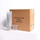 A brown cardboard box labeled 'MIXING CUP 385ML 200PCS' stands next to two stacks of clear plastic mixing cups with printed measurement markings on a white background.