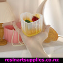 Hand holding a small resin mold with colorful resin pieces inside, on a decorative background.