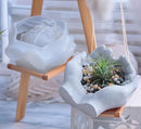 Decorative planters with a two handed resin mould design on a wooden stool.